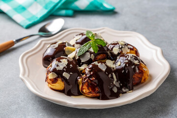 Delicious profiteroles with chocolate and white plate. Selective focus image on light background.