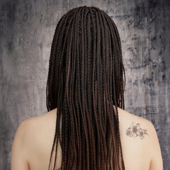Beauty and spa. A Caucasian woman's back with African braids and a discreet tattoo