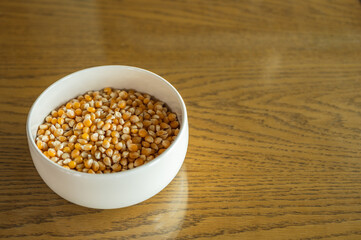 Corn kernels in white bowl on wooden pattern table top.