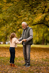 Fototapeta premium Grandfather spending time with his granddaughter in park on autumn day