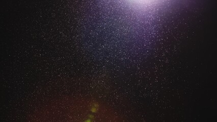 Natural dust particles floating on black background with light. Glittering particles in the air with effect bokeh. Macro shot of texture whites snow, smoke, steam, fog with purple glare luminosity.