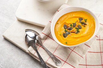 Two white soup bowls with creamy orange pumpkin soup or mash with pumpkin seeds on kitchen towel and marble board