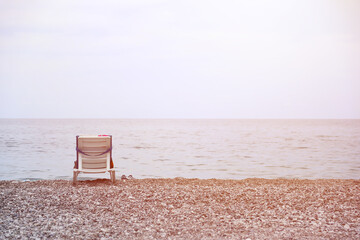 Chair on bank of pebbles with the sea and beach
