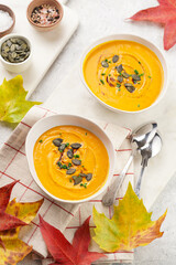 Two white soup bowls with creamy orange pumpkin soup or mash with pumpkin seeds on kitchen towel and marble board