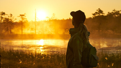woman tourist meets dawn in nature. Sunset,  light and fog, Reflections of trees in lakes . Travel...
