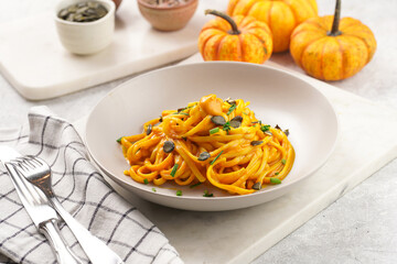 A light grey deep bowl with vegan pasta spaghetti carbonara with orange pumpkin sauce and fresh...