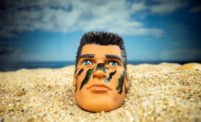 A male doll head buried in sand on beach 