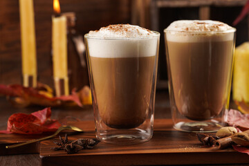 Two transparent glasses with cappuccino with black coffee, milk foam and cinnamon in autumn...