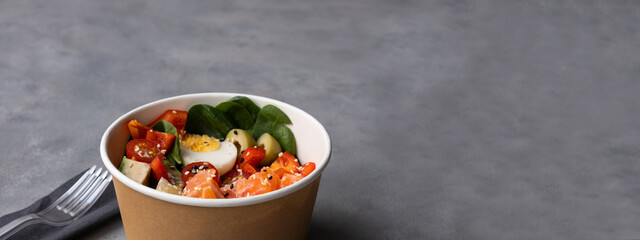 Takeaway poke bowl with fresh salmon, avocado, quinoa and vegetables in recycled kraft paper...