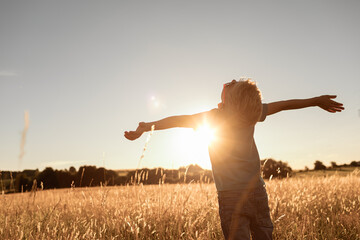 Don't worry be happy! Child standing in a field at sunset having feelings of freedom, hope, and...