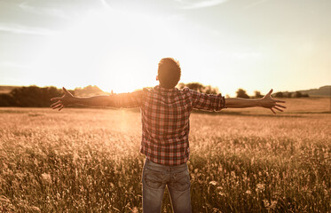 Happy young man feeling good letting go of worries and fears standing in a field with open arms up...