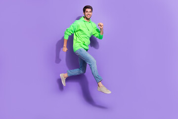 Fototapeta na wymiar Full length photo of good mood man wear green jumping high running fast isolated purple color background