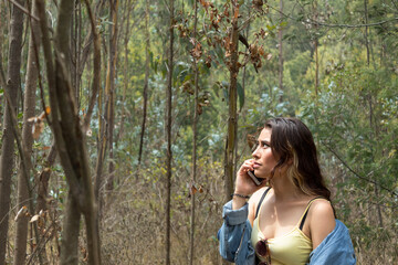 A young white woman lost in the woods calling on her cell phone on a hot day