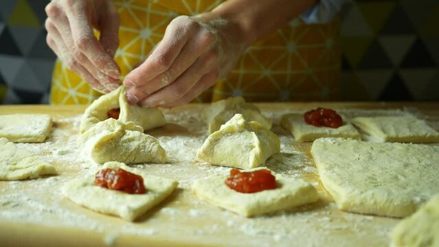 Women's hands in flour make a donut with jam. Close up process of making sweet round buns 