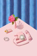 Retro vintage scene with old dial phone, rose flower and cigarette pack on bright pink table. Blue plush curtain background.