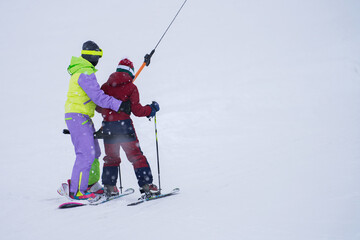 A woman and a child are towed uphill on a t-bar in a snowfall. Copy space. Selective focus.