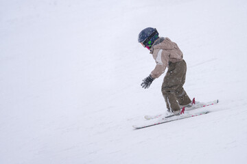 A little boy takes his first steps on downhill skiing. He clumsily and cautiously descends the...