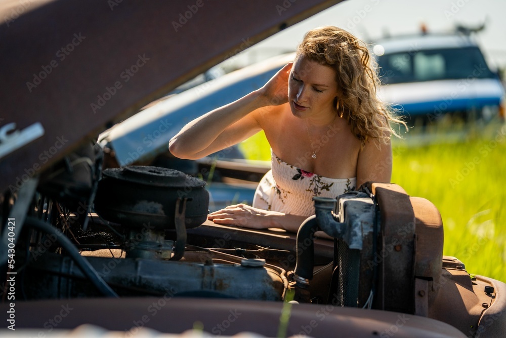 Wall mural pretty young caucasian female pretending to check the hood of a car in an auto wrecking yard