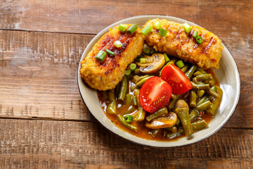 Green beans with champignons and homemade cutlets sprinkled with green onions with a fork on a wooden table.copy space