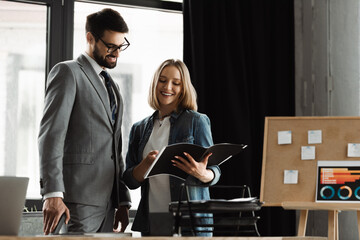 Cheerful woman holding resume near manager in suit during job interview in office.
