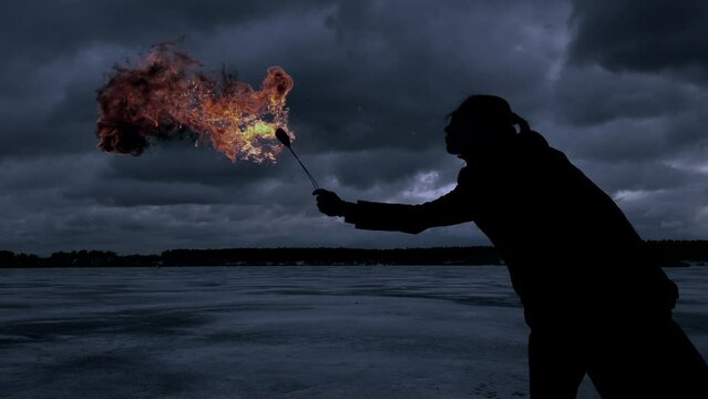 Fire show dark silhouette of a girl in a coat in winter against a sky with clouds dramatic film style slow motion 4K