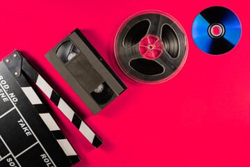 Compact disc, filmstrip bobbin, black plastic VHS video cassette and clapper board on pink...