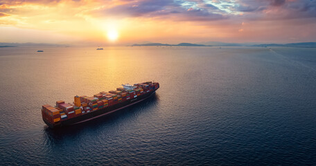 Aerial view of a large, heavy loaded container cargo ship sailing over calm sea into the sunset with copy space