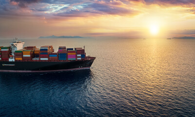 A cargo container ship sails over calm ocean into a golden sunset as a concept for global transport...