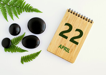 April 22. 22th day of the month, calendar date. Notepad, black stones, green leaves. Spring month, the concept of the day of year