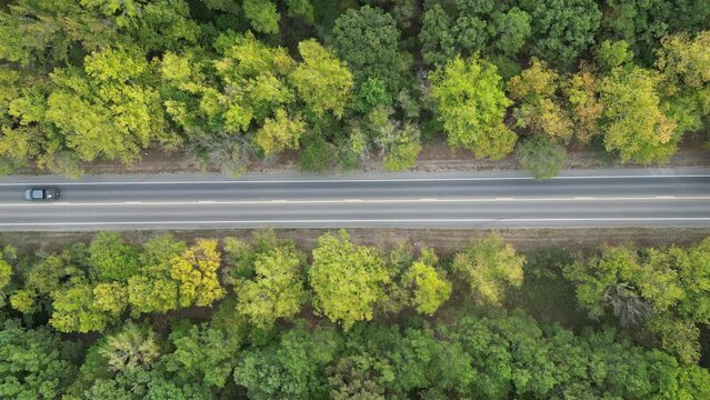 Aerial view from above of country road with moving cars through the green forest in Autumn, Broken Bow, Oklahoma, USA. Drone photography