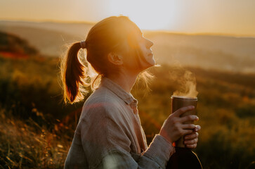 Silhouette of a woman enjoying hot cup of tea on hill at sunset	
