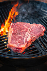Rohes Dry Aged Wagyu Porterhouse Steak vom Rind gegrillt als close-up auf einem Holzkohle Grill mit Feuer und Rauch
