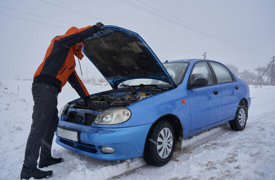 a man opened the hood of a car in winter,car broke down in the winter, man inspecting the car engin