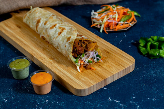 Paneer Tikka shawarma Wrap with salad dip and sauce isolated wooden board side view of fastfood