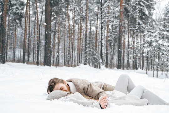 Romantic snow love story.Young couple guy girl lying,playing in snowy winter forest with trees.Walking, having fun, laughing in stylish warm clothes, fur coat,woole jacket,shawl.Date,vacation weekend