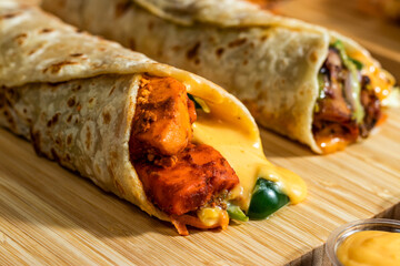 Melt Cheese Paneer Wrap, Chicken Afghani Kebab shawarma Wrap with salad dip and sauce isolated wooden board side view of fastfood