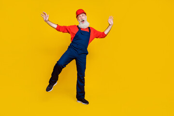 Photo of cheerful good mood senior guy dressed uniform overall red hardhat having fun dancing isolated yellow color background