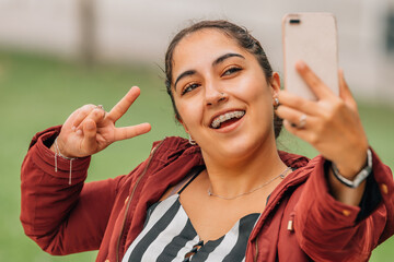 young woman with braces with mobile phone waving happy