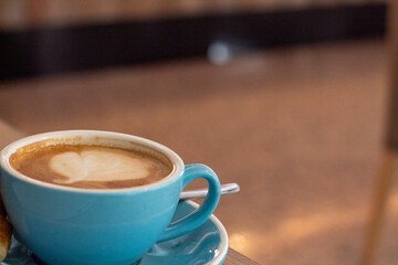Café con leche en una taza grande azul con un mini cruasán mientras teletrabajas en una cafetería de Alicante con el fondo desenfocado. 