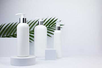 Set of white cosmetic bottles mockup with palm leaf. White plastic bottles with shampoo and conditioner and shower gel on a white background. Mockup cosmetic bottle on white background