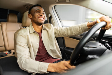  Portrait of happy african american man driving car with beige interior - Powered by Adobe