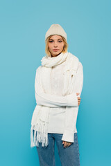 young blonde woman in white sweater and winter hat standing isolated on blue.