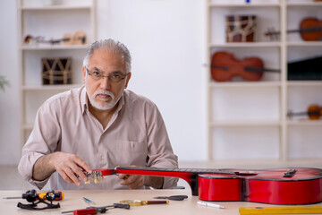 Old male repairman repairing musical instruments at workshop