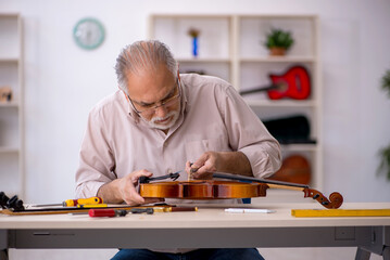 Old male repairman repairing musical instruments at workshop