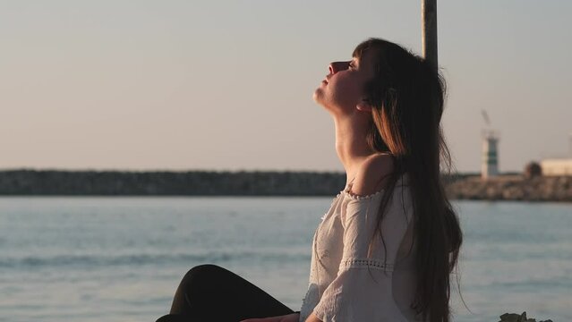 girl sits by the sea and relaxes feeling the sun on her face
