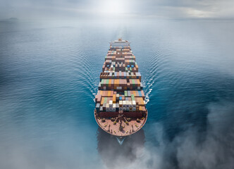 Aerial top view of a big cargo container ship traveling over the calm ocean with fog and clouds