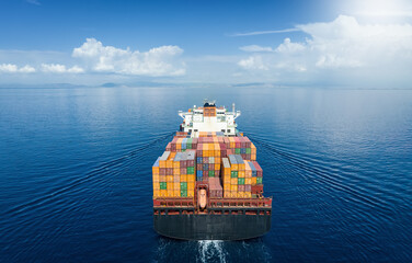 Aerial back view of a large container cargo carrier ship traveling over very calm ocean with...