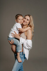 Portrait of happy mother with son standing at studio. Attractive pregnant woman with curly hair, holding her little son on hands and looking at camera