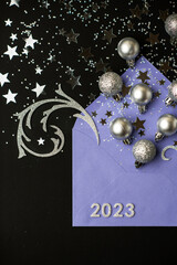 Happy New Year 2023. Purple envelope with silver Christmas balls and sparkling glitter confetti on black background. Сhristmas flat lay.