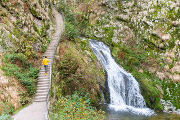 Ein Mann läuft neben einen Wasserfall  im Herbst im Schwarzwald